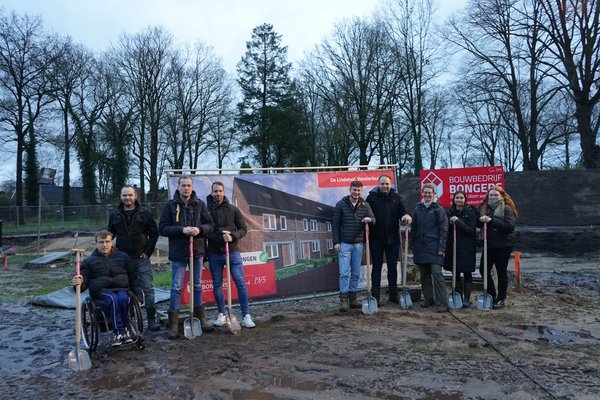 8 kopers van de kavels staan samen met wethouder Rieja Raven met een schep in de hand op de plek waar de woningen moeten komen. 