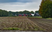 Lievingerveld vanuit de verte. Op de voorgrond een akker. In de verte een aantal huizen, waaronder een rood houten huis.